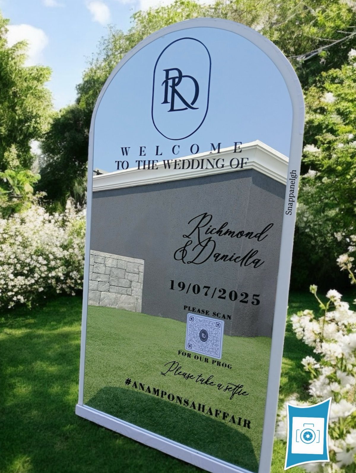 Arched wedding welcome sign on a green lawn with white floral surroundings.