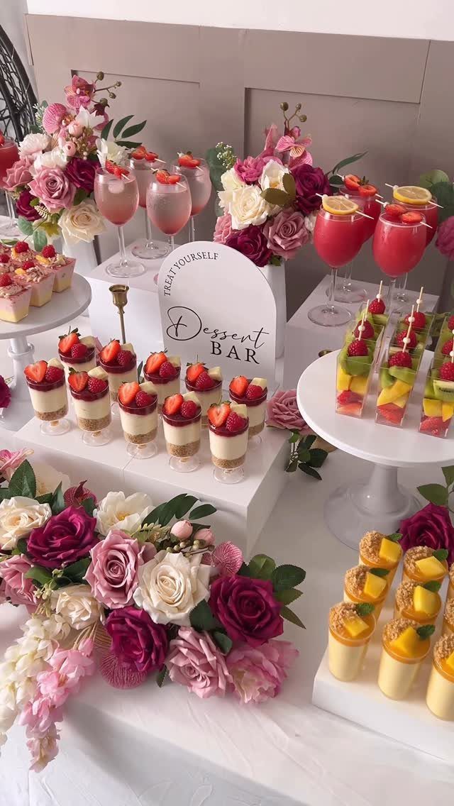 Dessert bar with strawberry parfaits, fruit skewers, and pink roses on white table