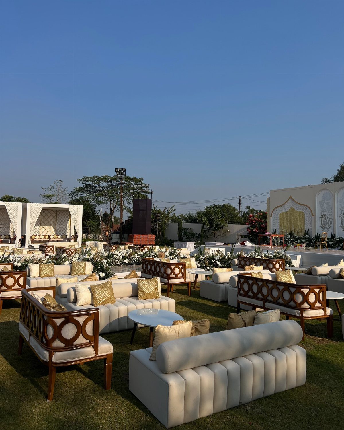 White upholstered lounge seating with gold pillows arranged on a green lawn.