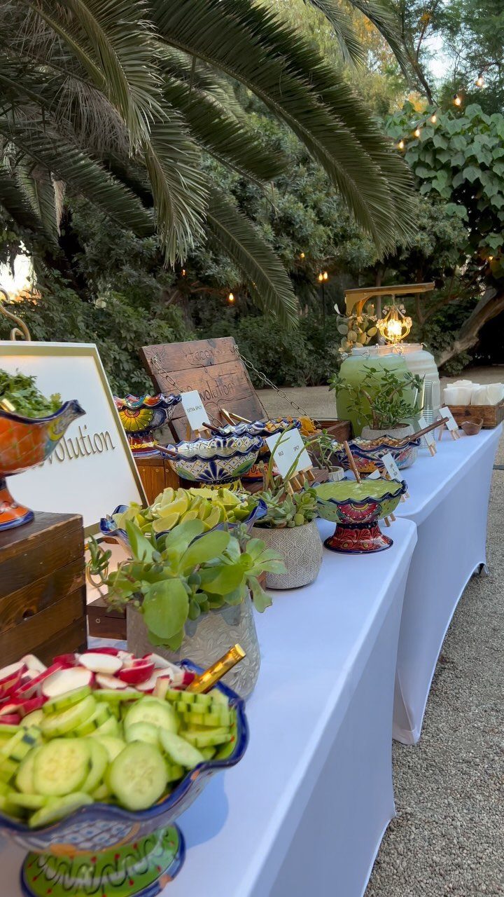 Buffet table with colorful bowls of appetizers set outdoors under palm trees