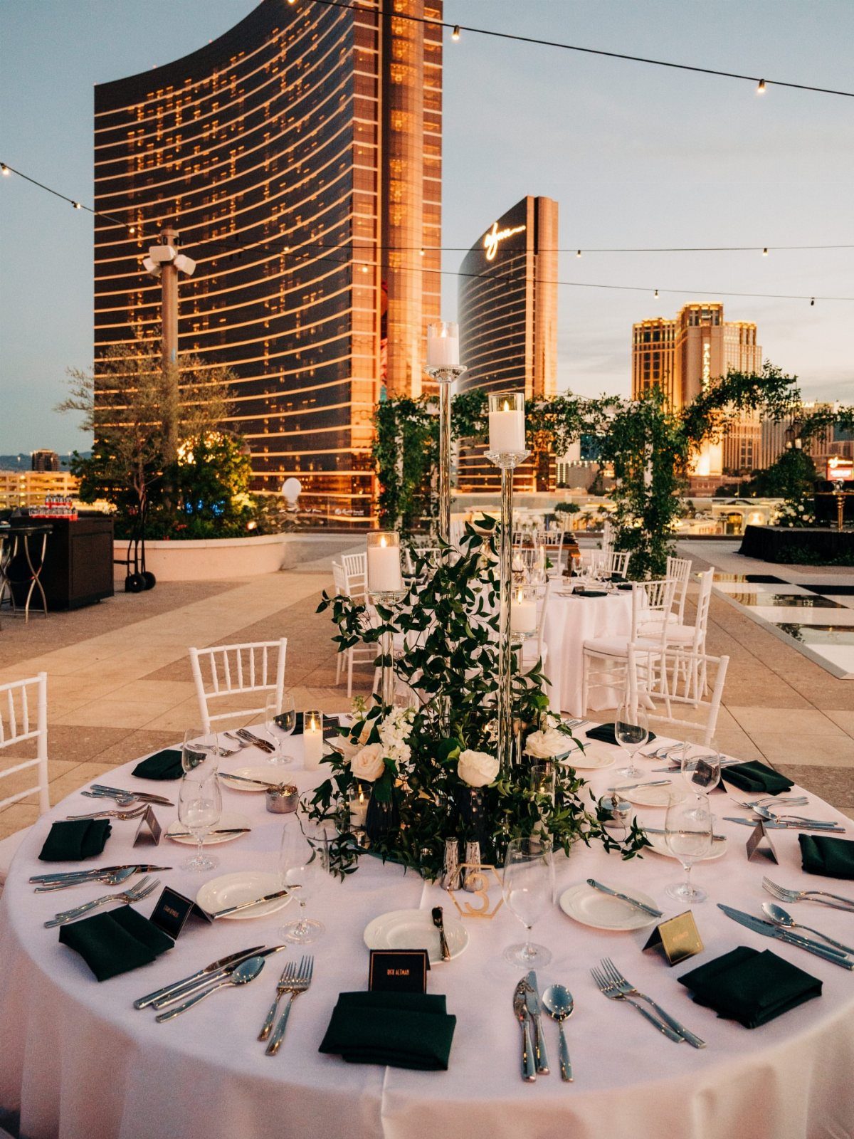 Formal dinner table on a rooftop terrace overlooking gold skyscrapers in a city.