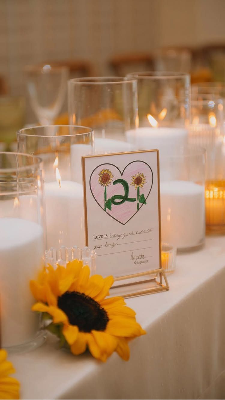 Table number card with sunflowers and a heart among white candles and sunflowers.