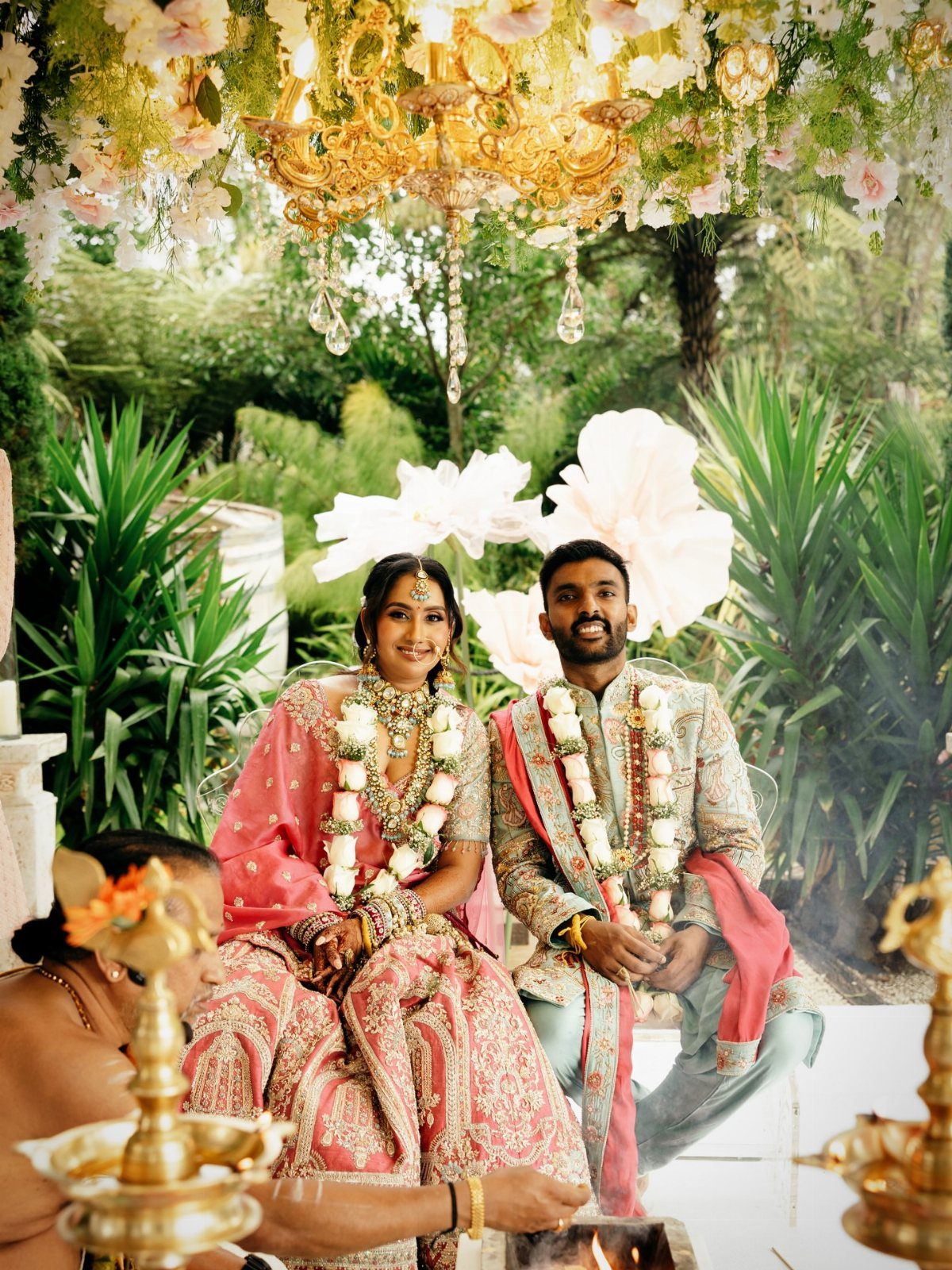 Indian couple in traditional wedding attire sitting during a ceremony under floral canopy