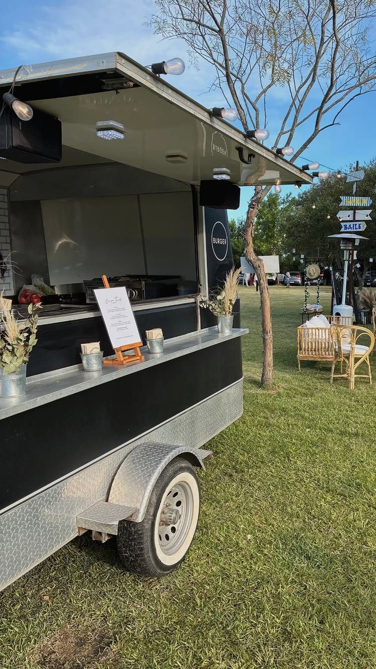 Black and silver food truck with string lights parked on a grassy field