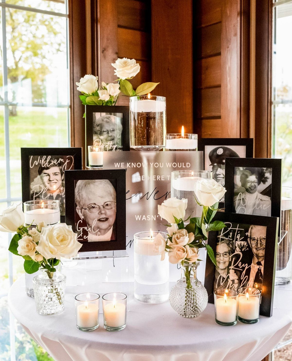 Memory table with framed portraits, white roses, and lit candles on white tablecloth