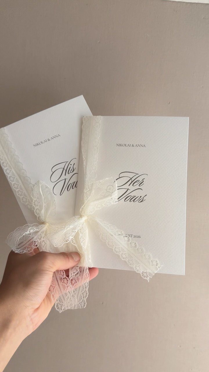 Two white vow booklets tied with a lace ribbon held by a hand.
