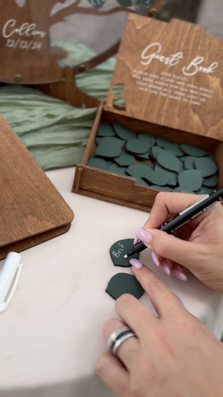 Hands writing on green wooden discs for a unique wedding guest book setup