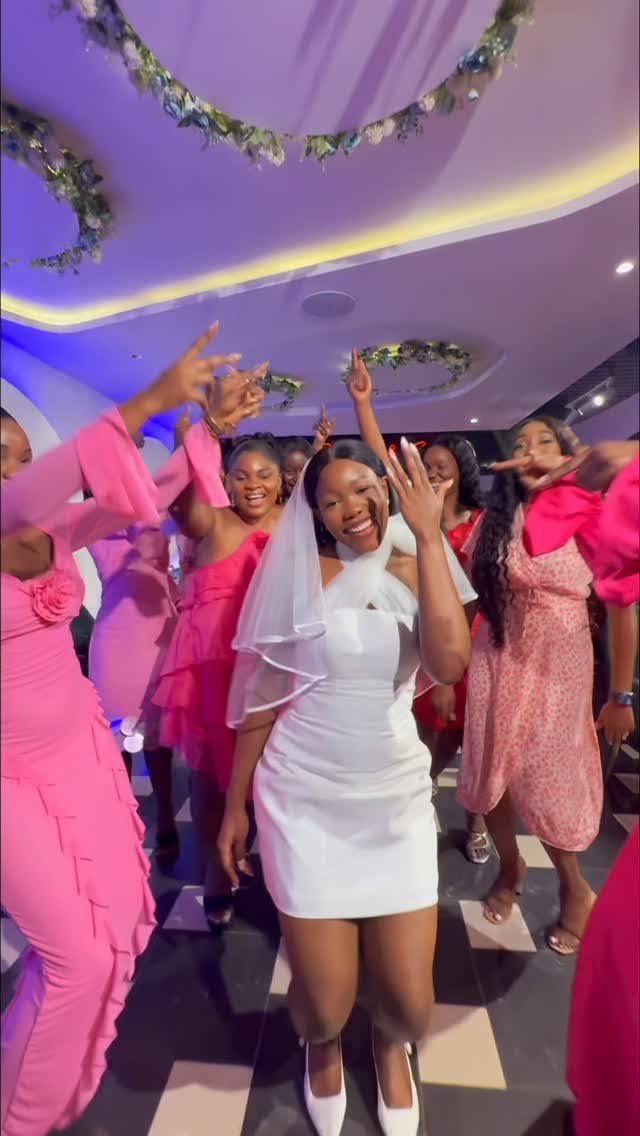 Woman in white dress and veil smiling with friends in pink dresses.