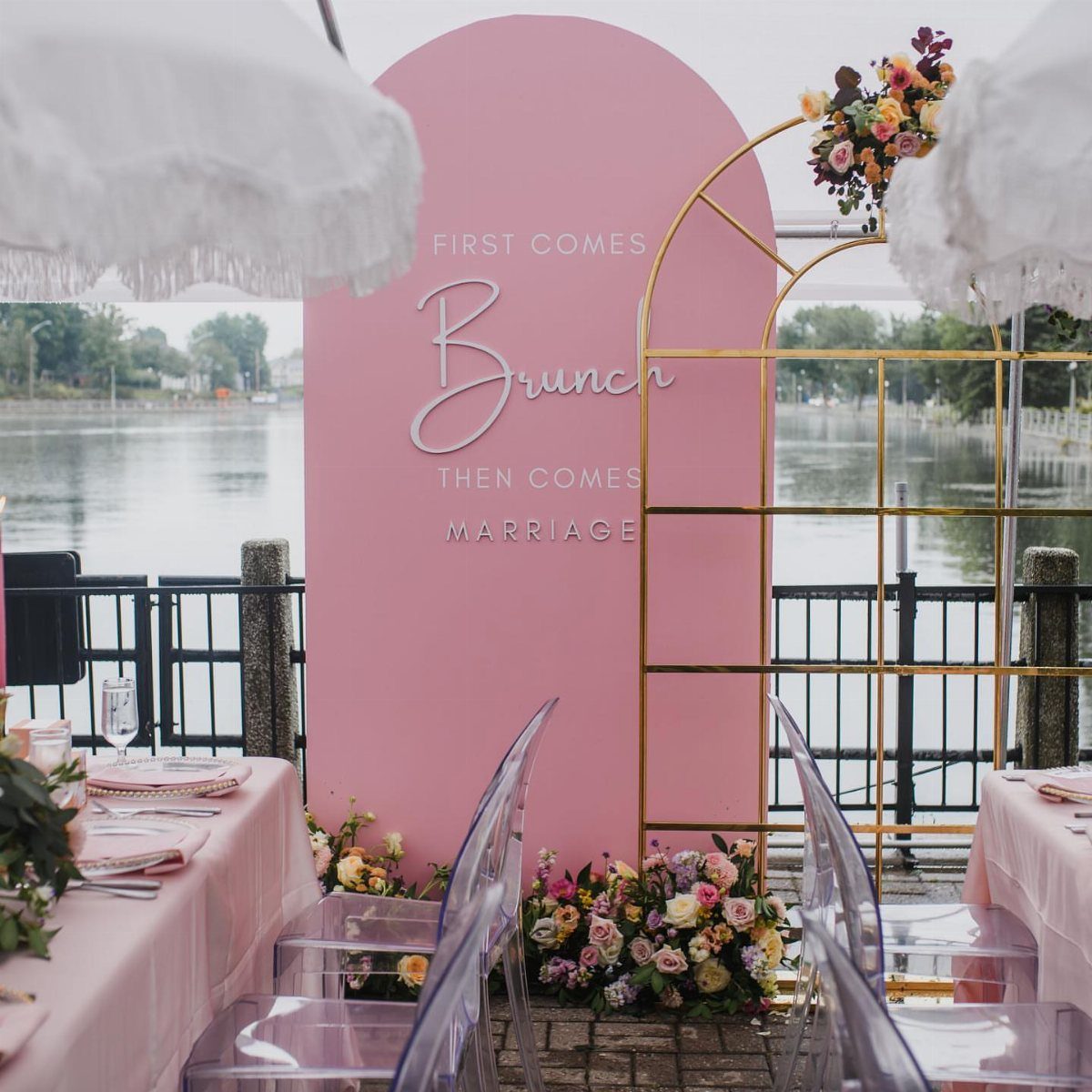 Pink arched backdrop with brunch text next to a decorated waterfront table.