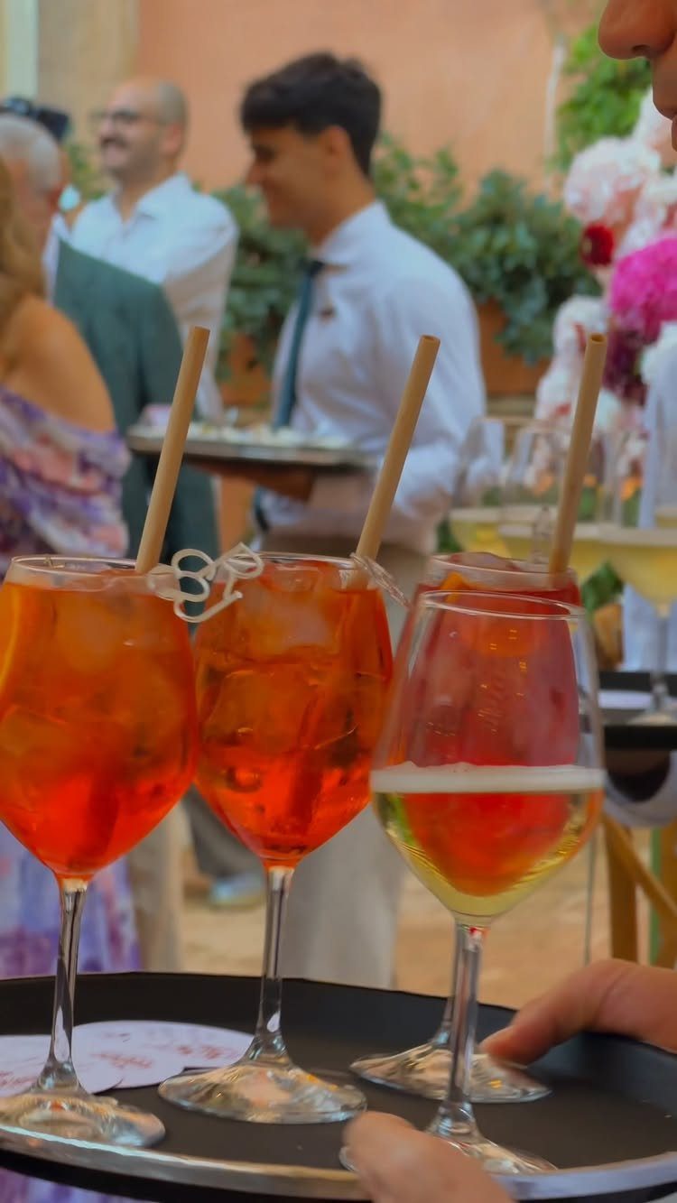 Orange cocktails on a tray with guests and a waiter in the background.