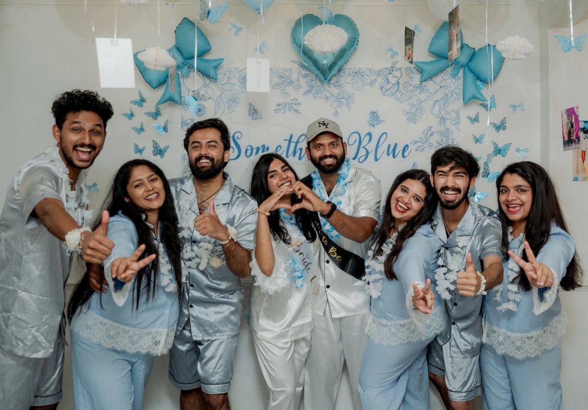 Group of friends in blue and white satin pajamas posing against blue decorations.