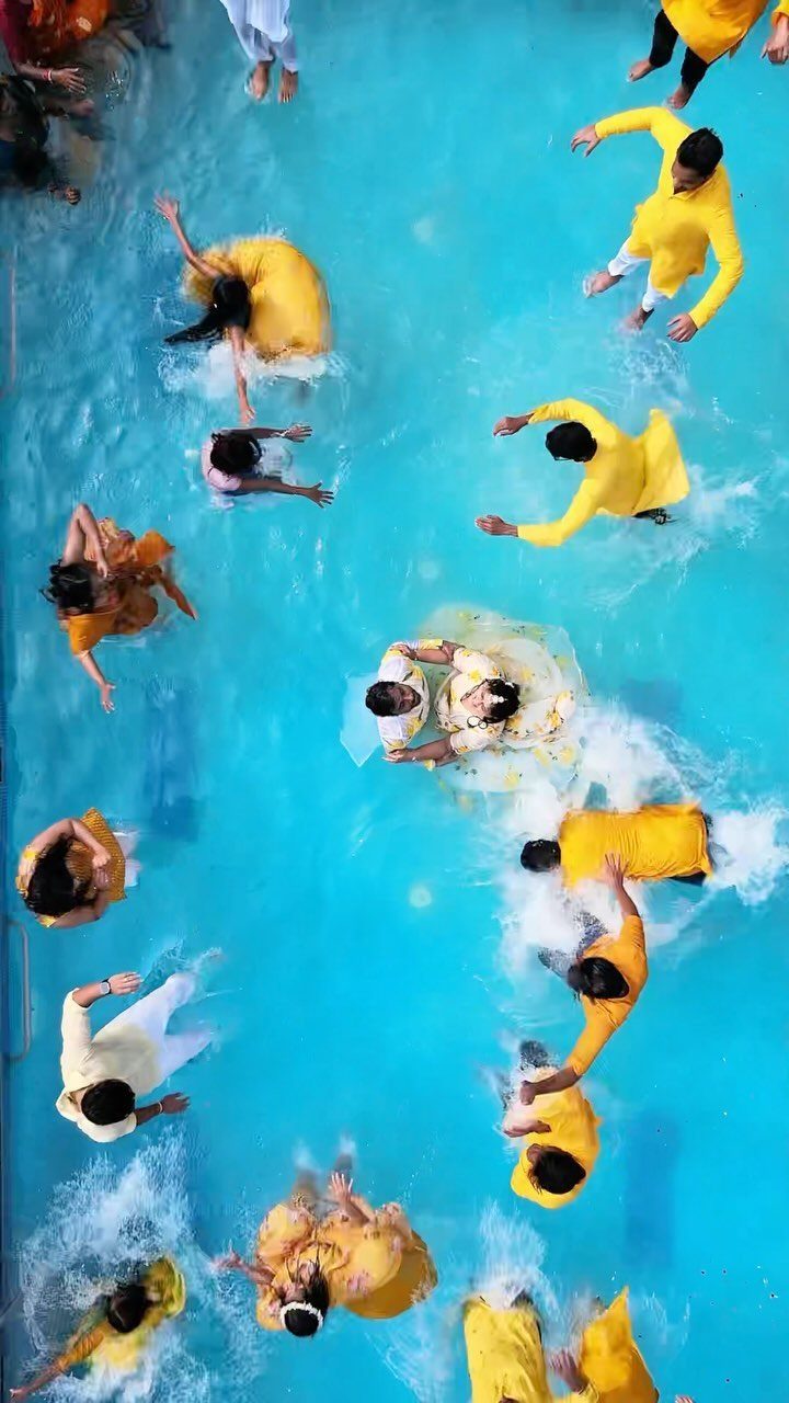 People in yellow traditional Indian clothing splashing and celebrating in a blue swimming pool.