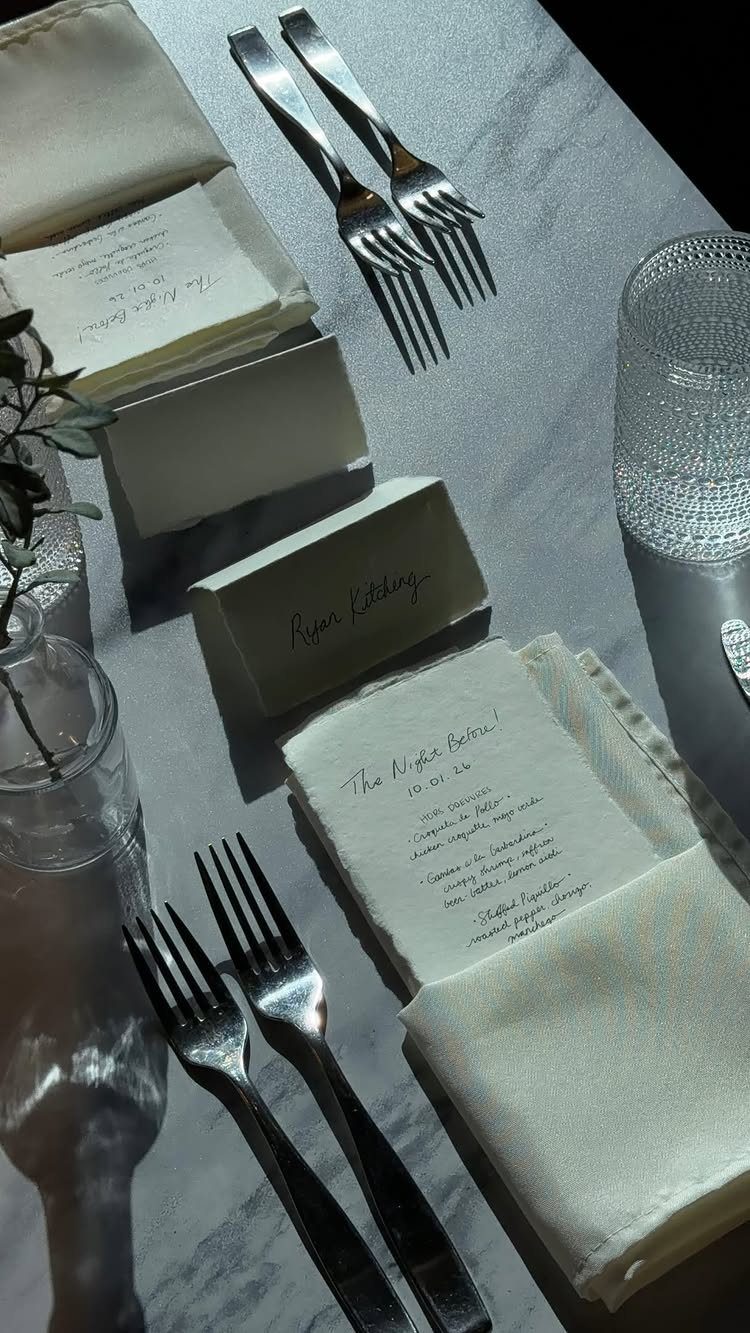 Formal table setting with silver forks, white napkins, and printed menu cards on marble.