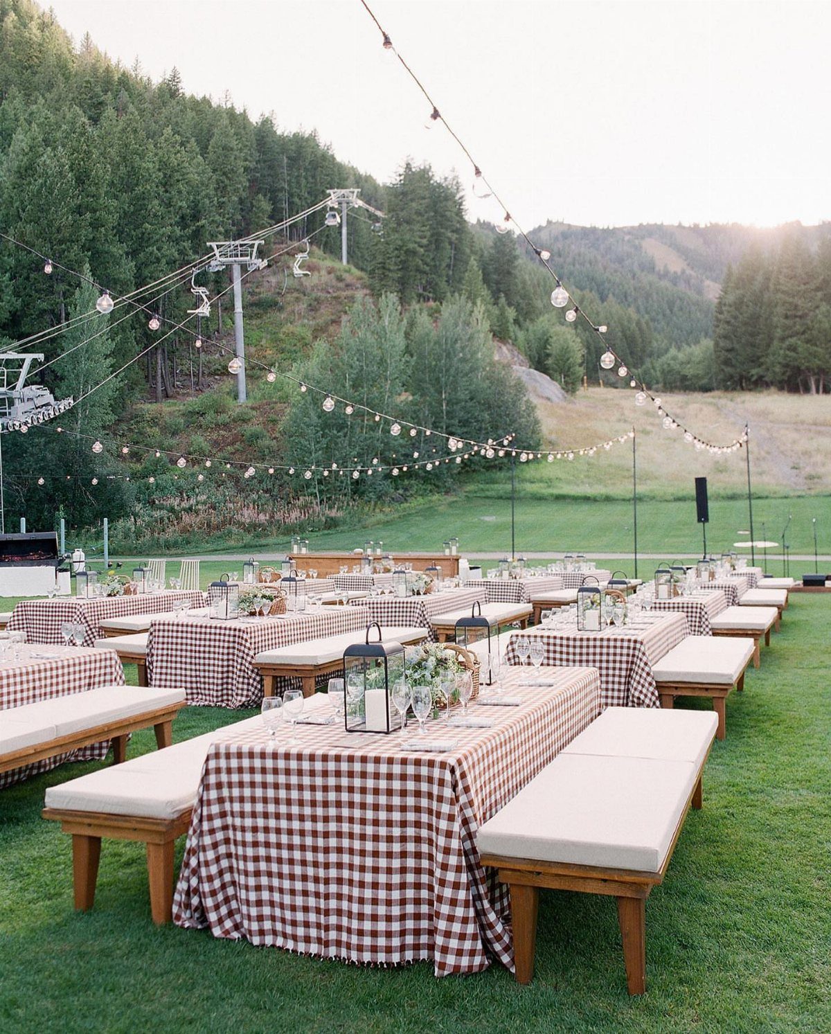 Outdoor dining tables with red checkered cloths and lanterns in a mountain setting.
