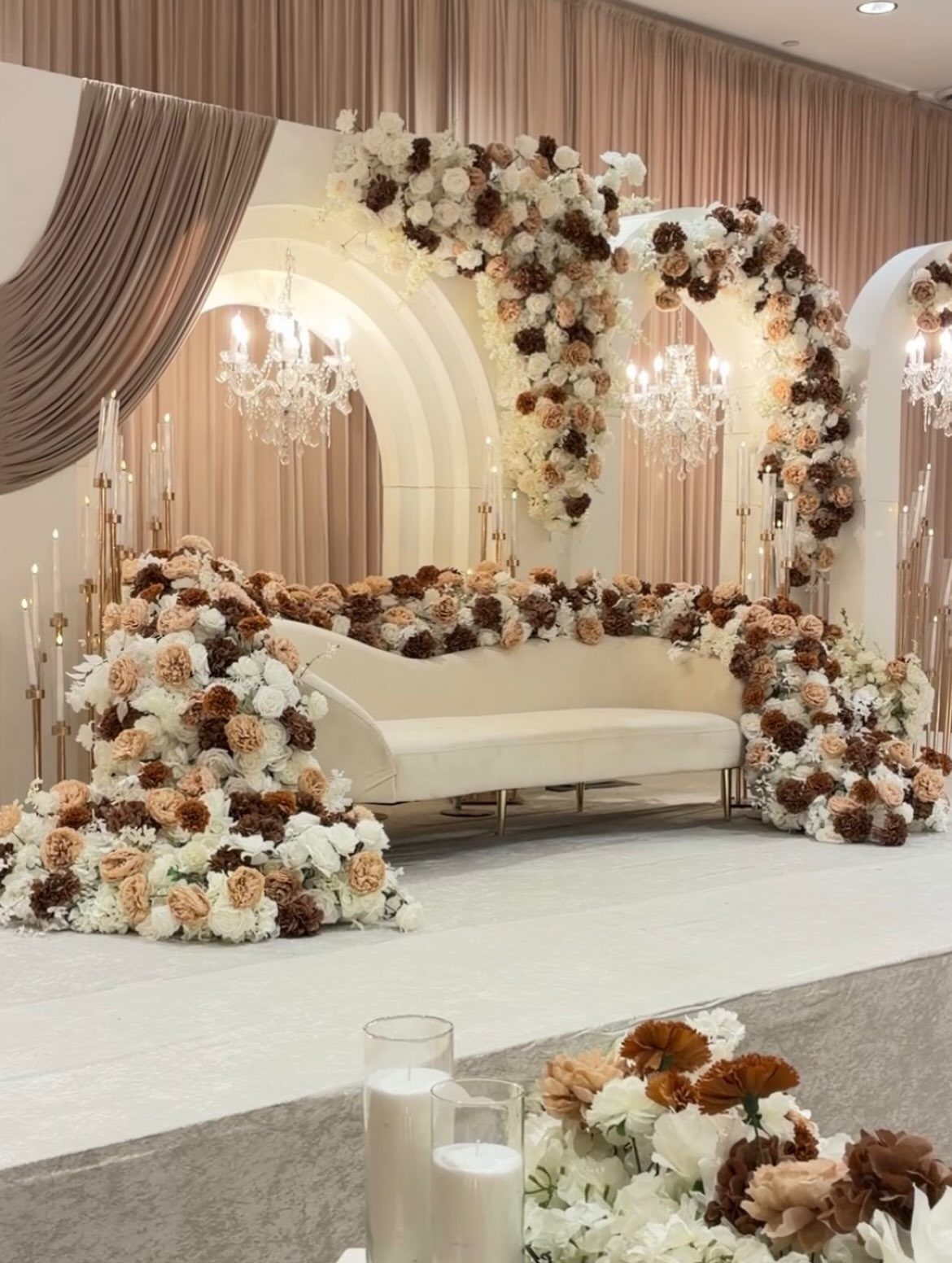 White curved sofa surrounded by abundant white and brown floral arrangements on a stage