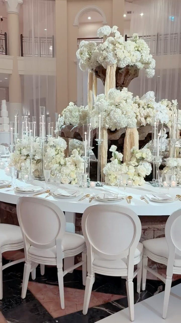 Towering white floral centerpieces on a white wedding table with elegant white chairs.