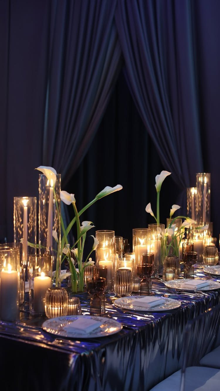 Dark blue satin table linens with white calla lilies and glowing cylinder candles.