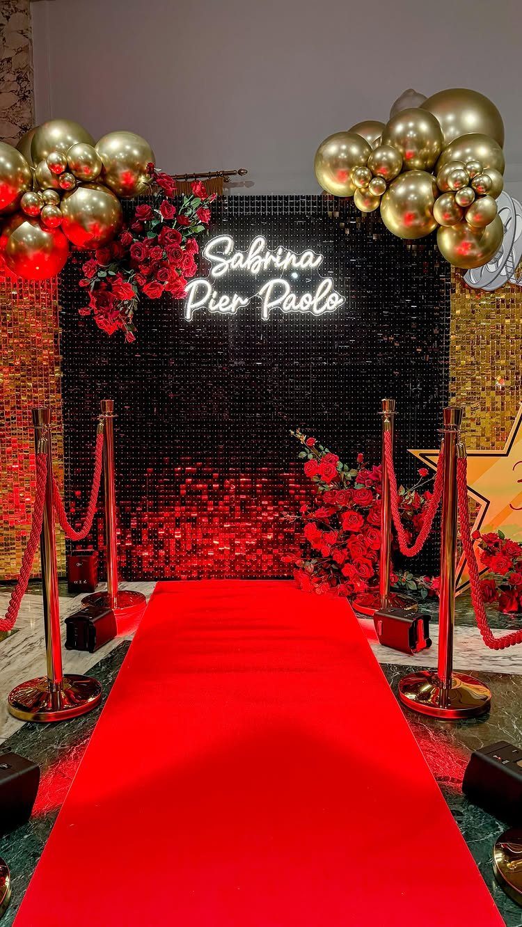 Red carpet leading to a black sequin wall with gold balloons and neon names.