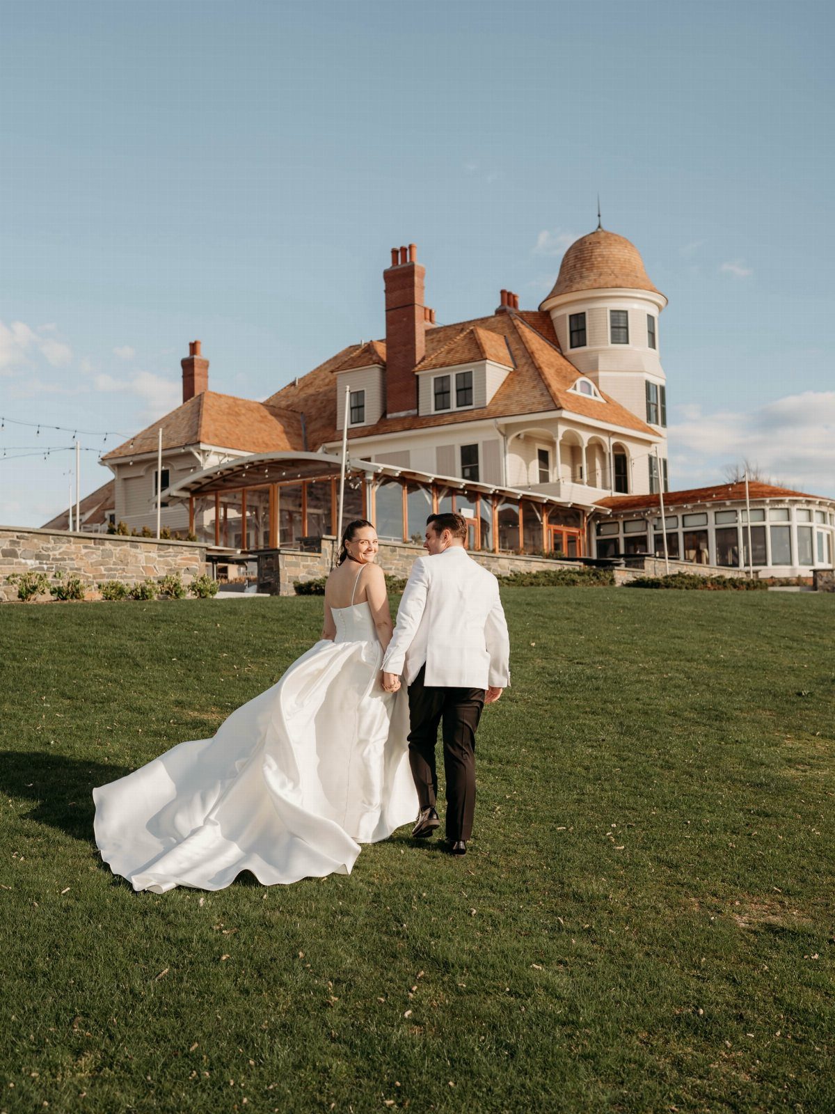 Bride and groom walking toward the historic Castle Hill Inn mansion on a lawn