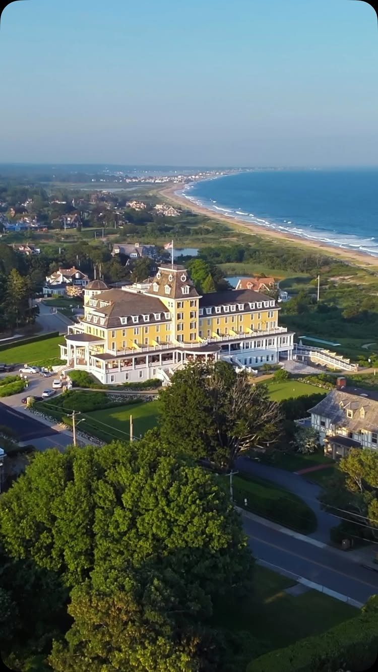 Large yellow historic coastal hotel overlooking a sandy beach and blue ocean shoreline.