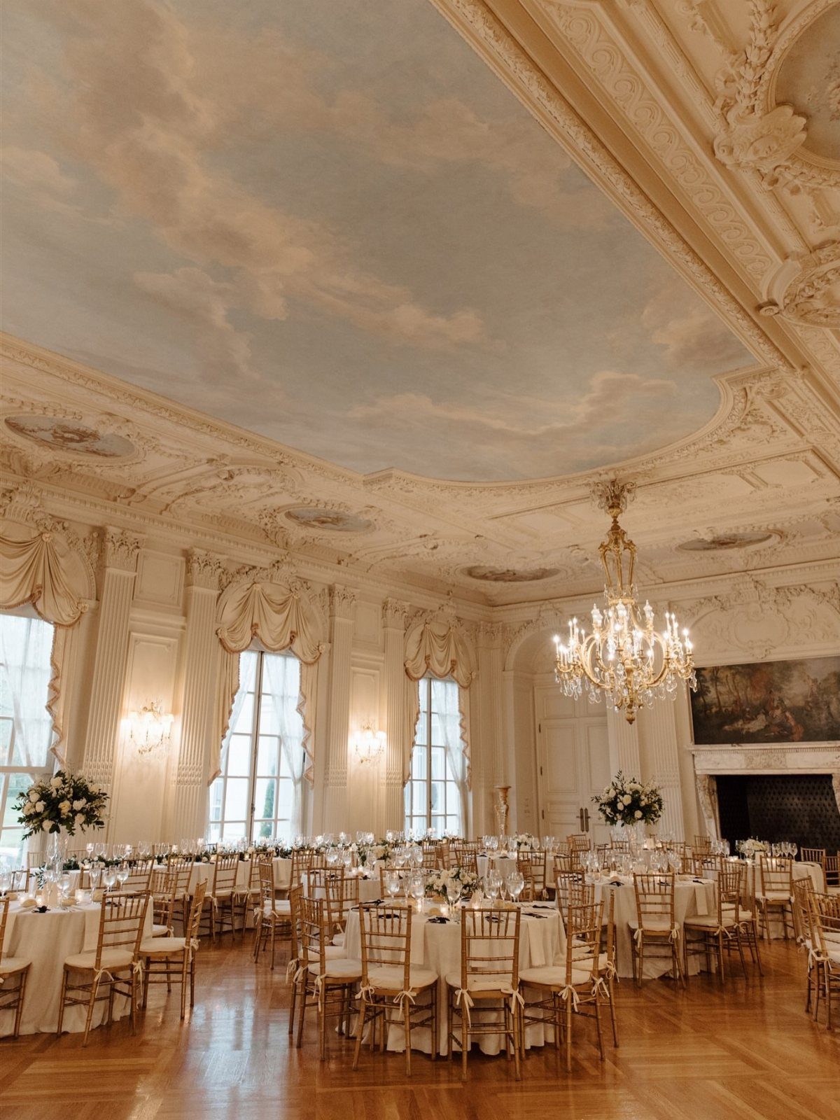 Opulent ballroom with painted sky ceiling and gold chairs set for a wedding.