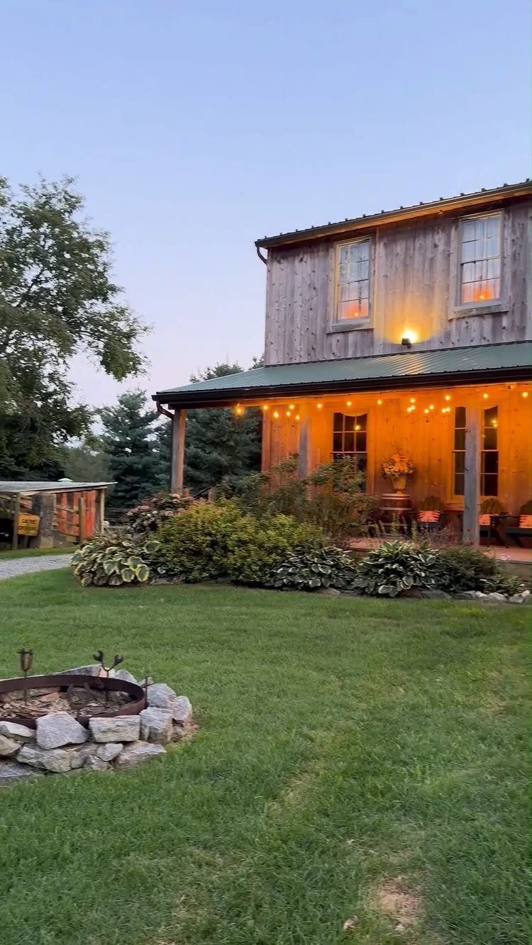 Rustic wooden barn with string lights and a stone fire pit on green grass