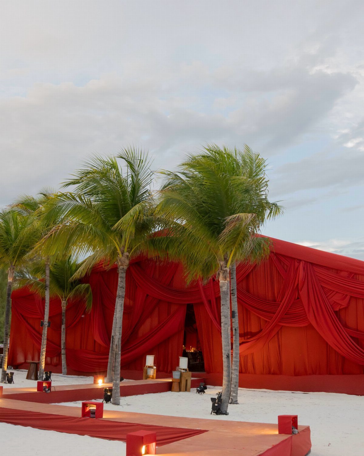 Red draped wedding tent on a white sand beach with palm trees.