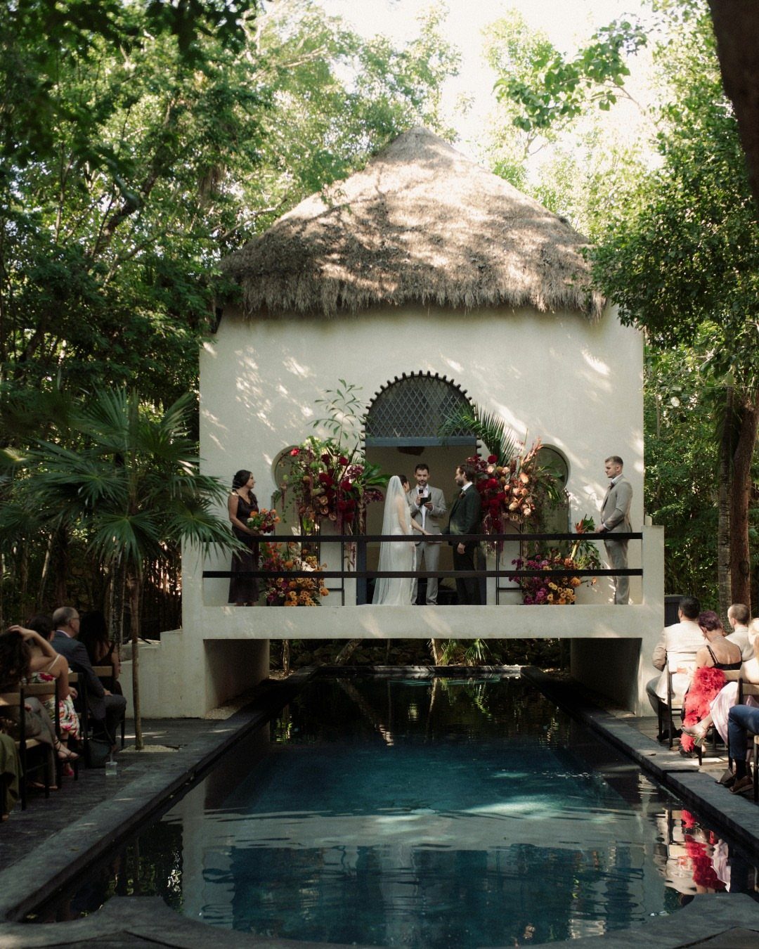 Wedding ceremony on a thatched-roof balcony overlooking a pool surrounded by tropical greenery