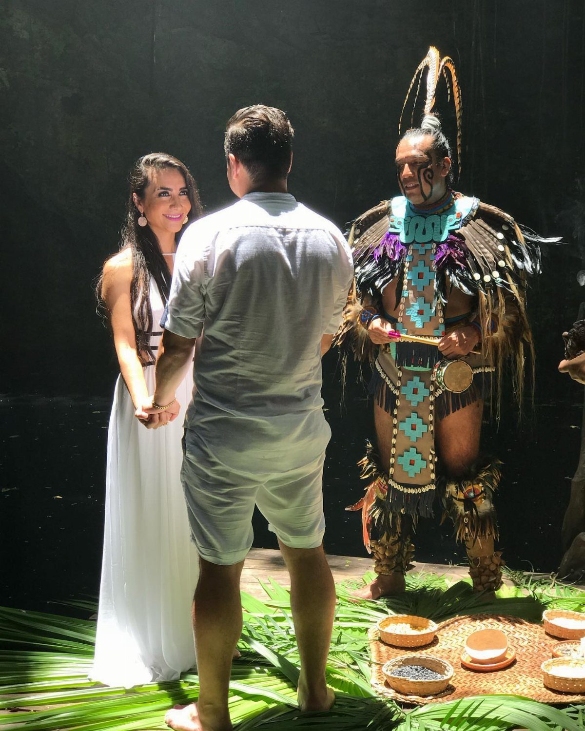 Couple in white wedding attire during a Mayan ceremony with a traditional officiant.