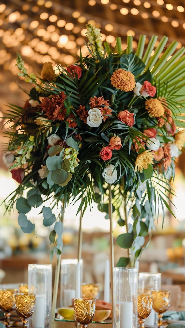 Tropical floral centerpiece with orange and white flowers on a gold stand.
