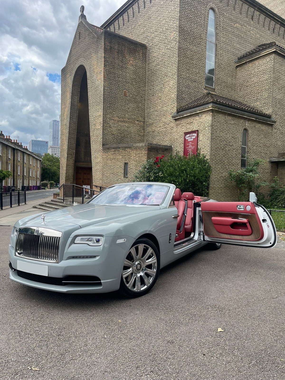 Grey Rolls-Royce convertible with red interior parked before a stone church building.