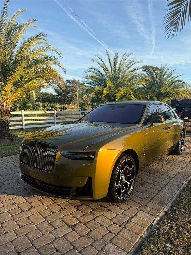 Gold Rolls-Royce luxury sedan parked on a cobblestone driveway with palm trees.