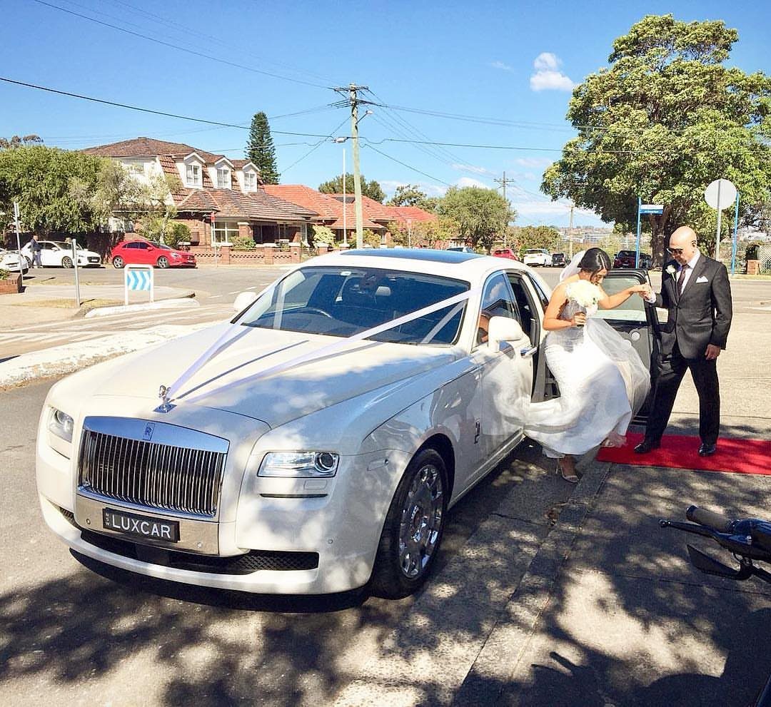 Bride stepping from a white Rolls-Royce onto a red carpet with a chauffeur.