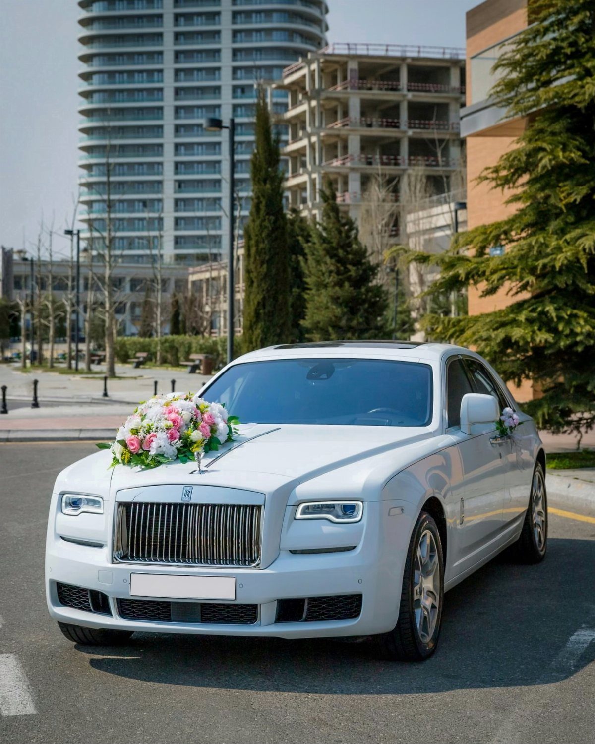 White Rolls-Royce decorated with pink and white floral arrangements for a wedding.