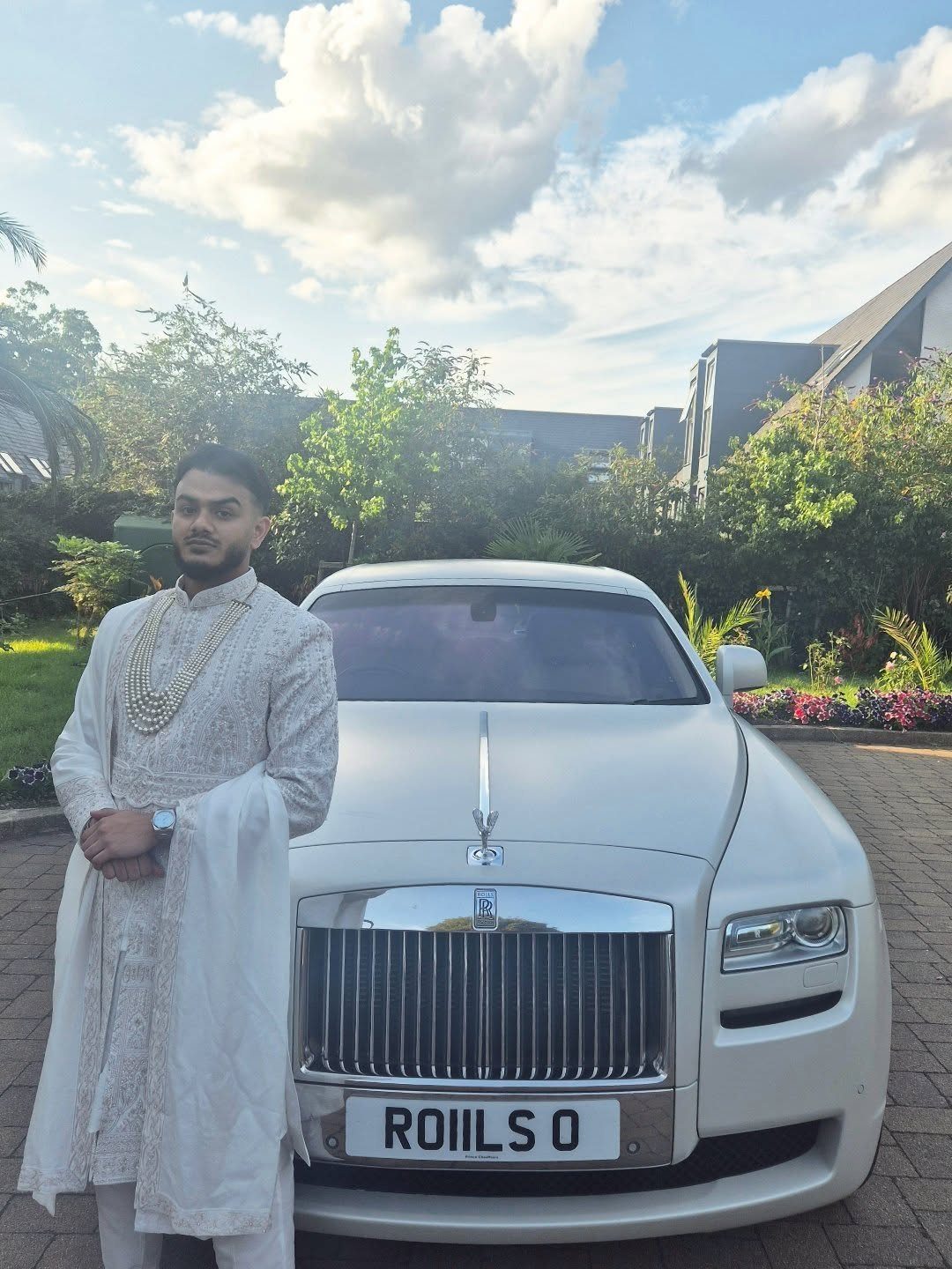 Man in white traditional wedding attire standing next to a white Rolls-Royce car.