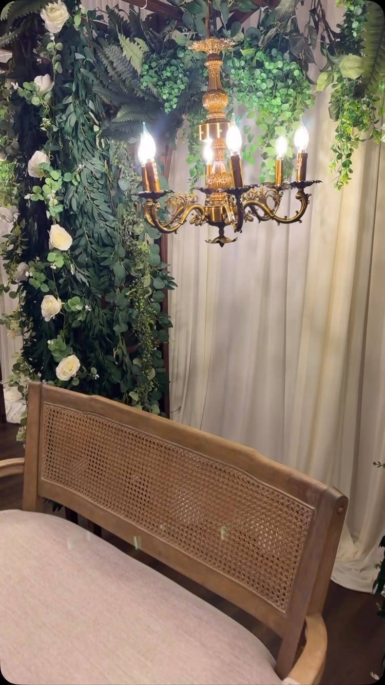 Vintage wooden cane settee with a gold chandelier and floral backdrop.