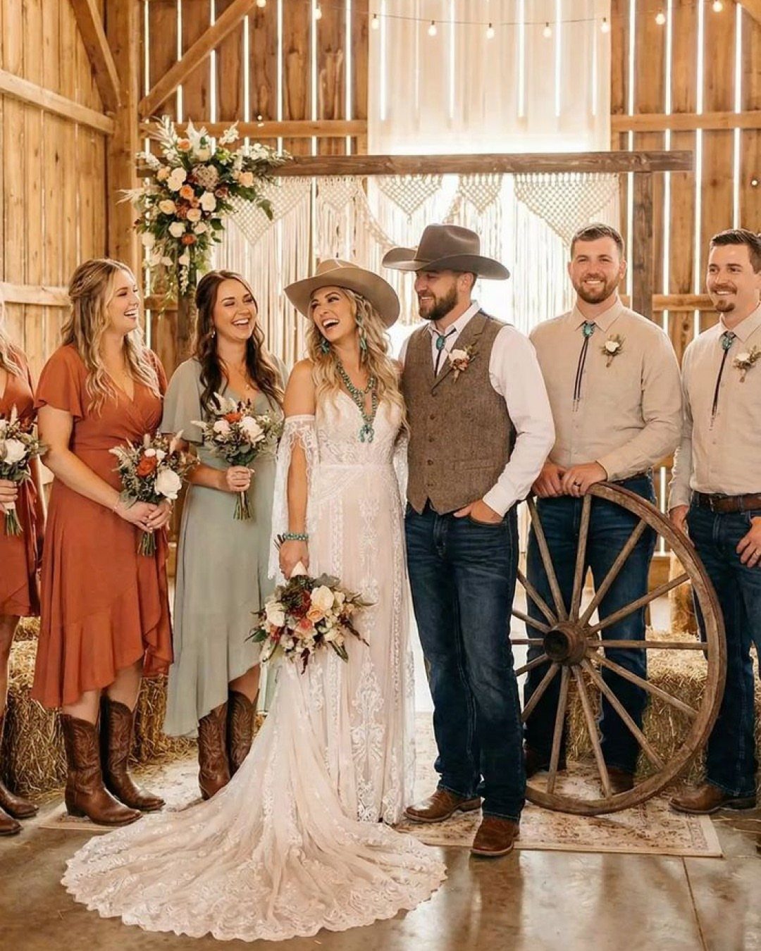 Wedding party in a barn wearing lace gown, vests, and cowboy boots.