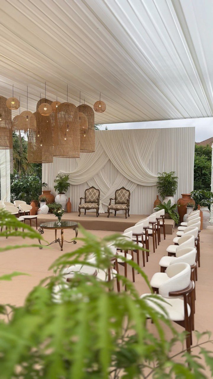 Outdoor wedding ceremony venue with white draped canopy, ornate chairs, and woven lighting.