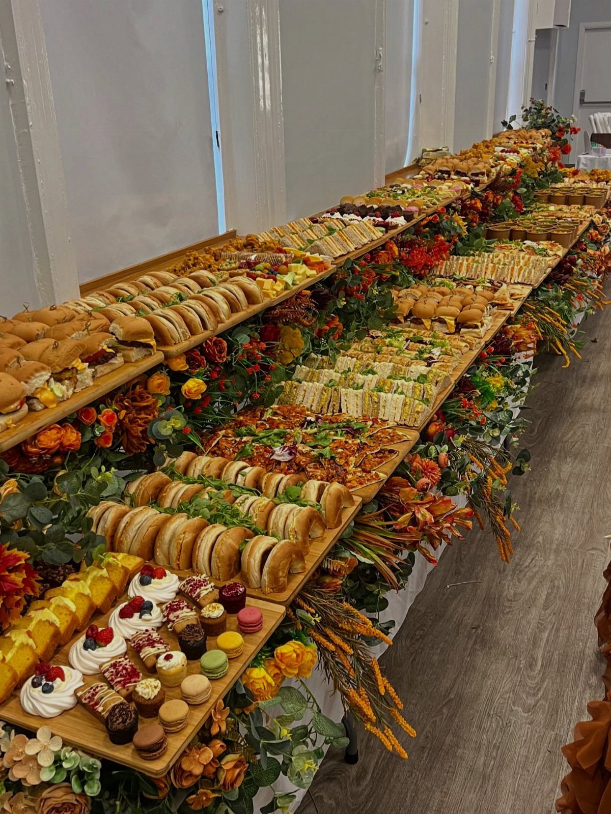 Buffet table with sliders and desserts decorated with autumn flowers and wooden boards