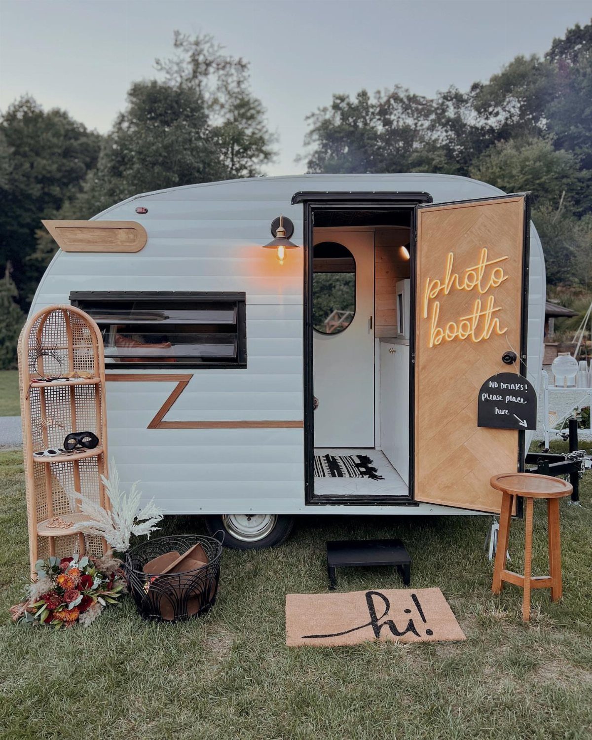 Vintage white camper trailer converted into a rustic photo booth on a grassy lawn.
