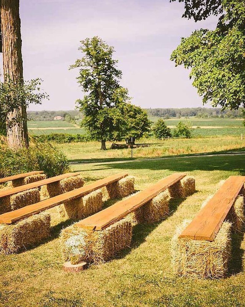 Wooden plank benches on hay bales in a grassy outdoor wedding setting