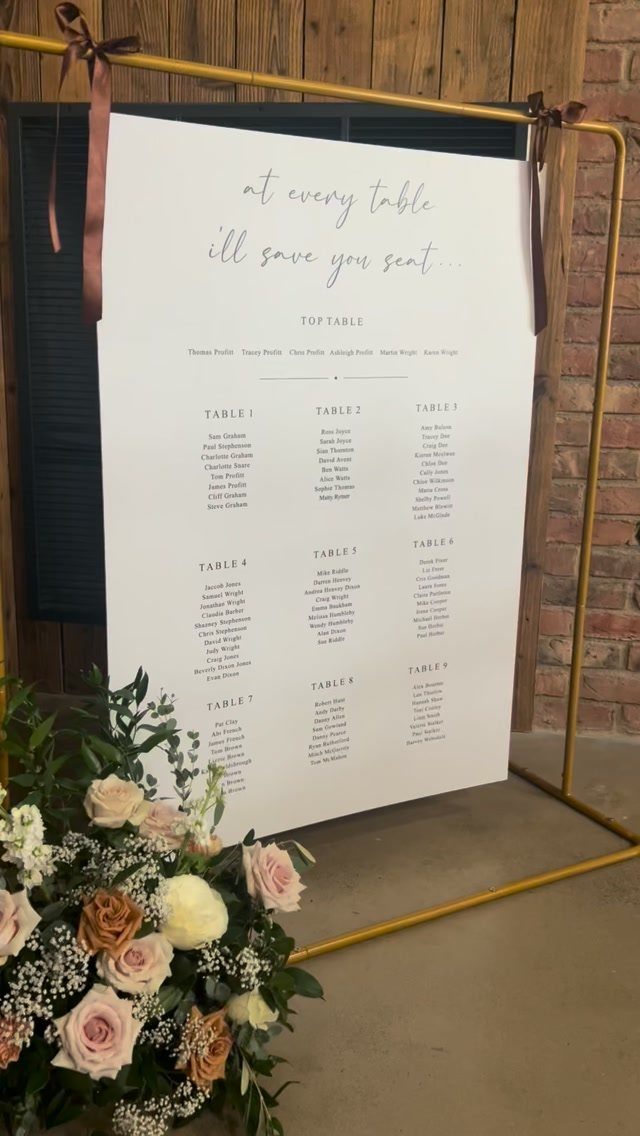 White wedding seating chart on a gold frame with roses and wooden background