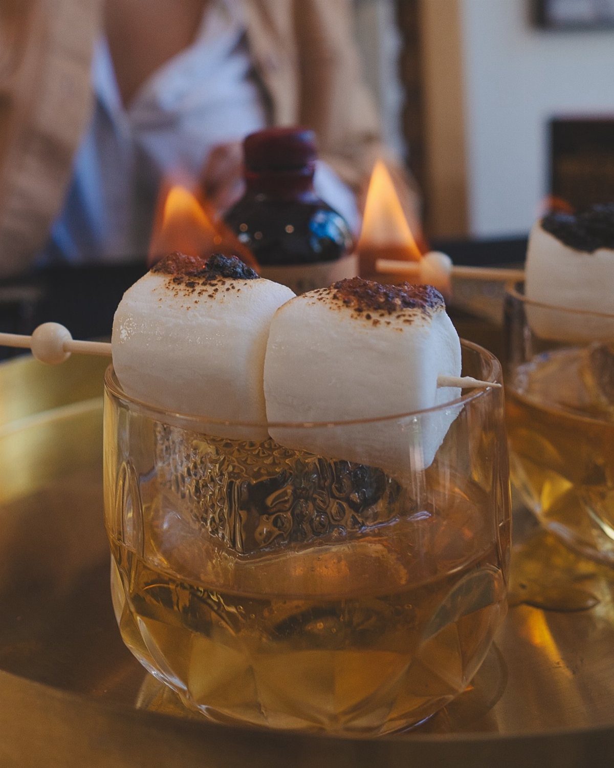 Amber cocktail in a crystal glass topped with toasted marshmallows on a skewer