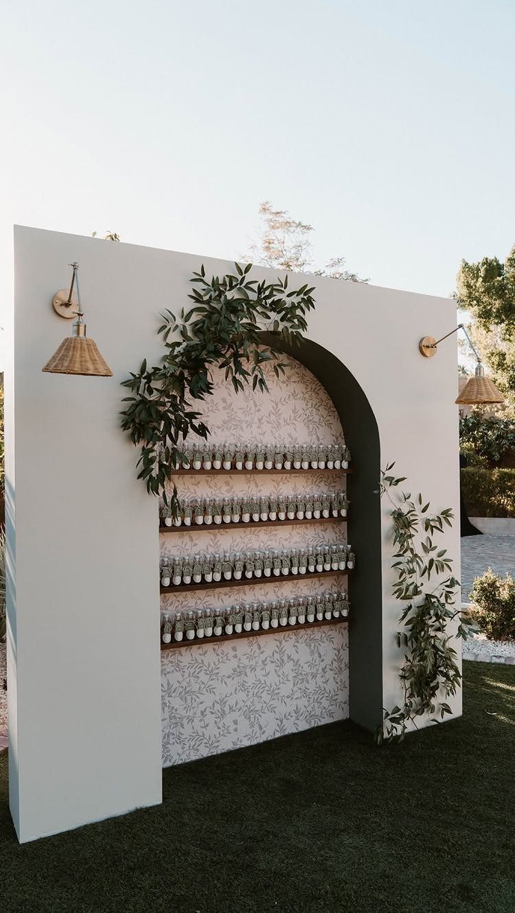 Arched white wall with shelves of small bottles and green leafy vines outdoors.