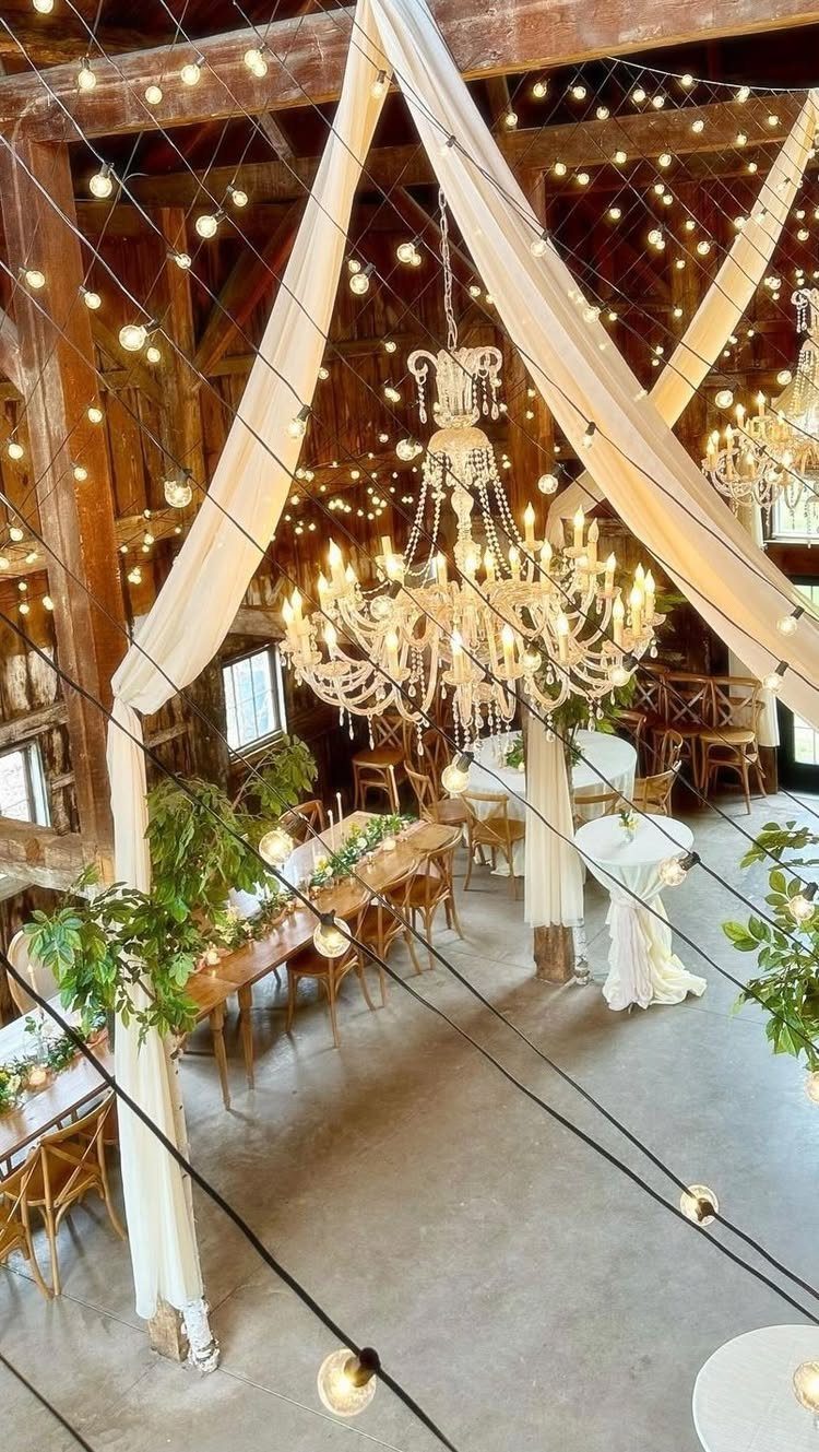 Rustic barn wedding venue with crystal chandeliers, white fabric draping, and wooden tables.