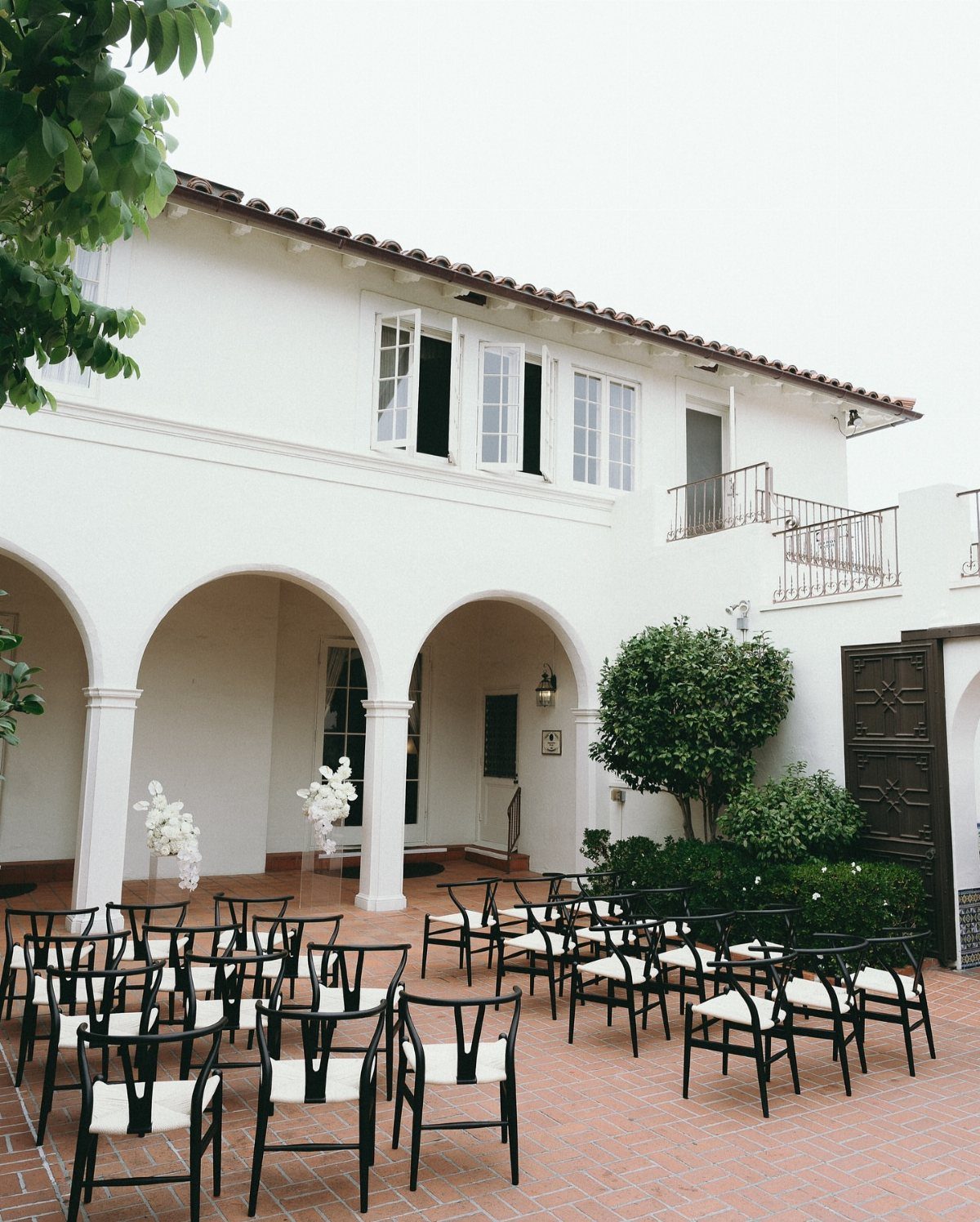 White Mediterranean villa courtyard with black chairs arranged for a wedding ceremony.