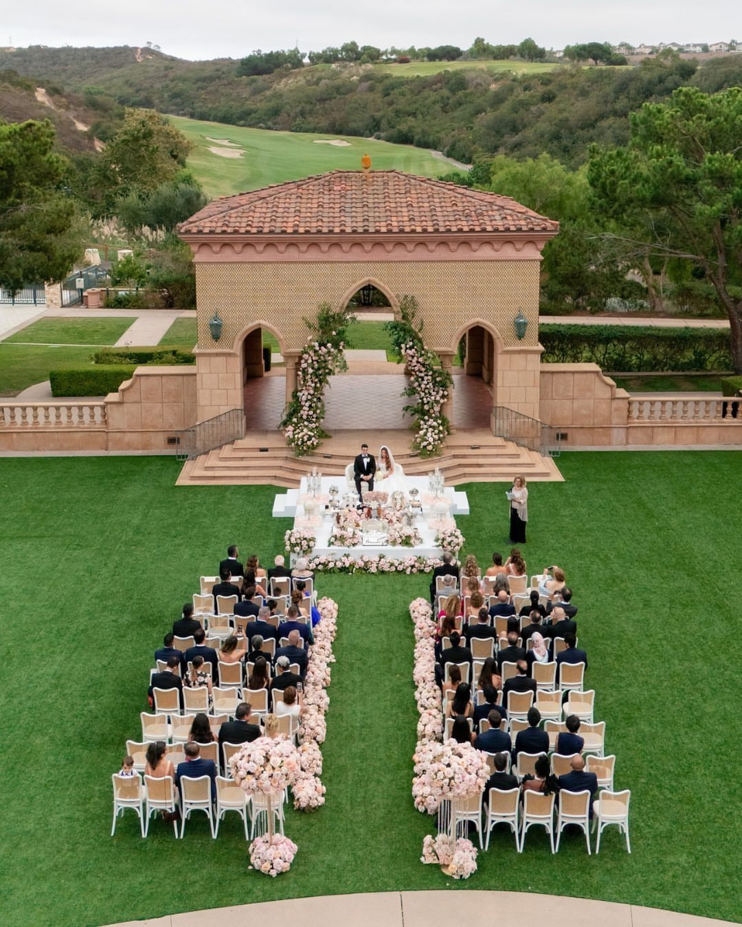 Outdoor wedding ceremony at Fairmont Grand Del Mar with guests and floral arch.