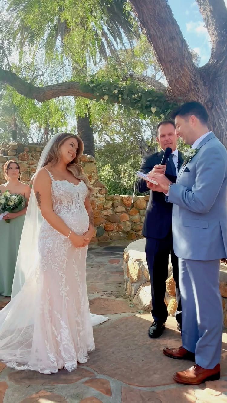 Bride and groom facing each other during an outdoor wedding ceremony under a tree.