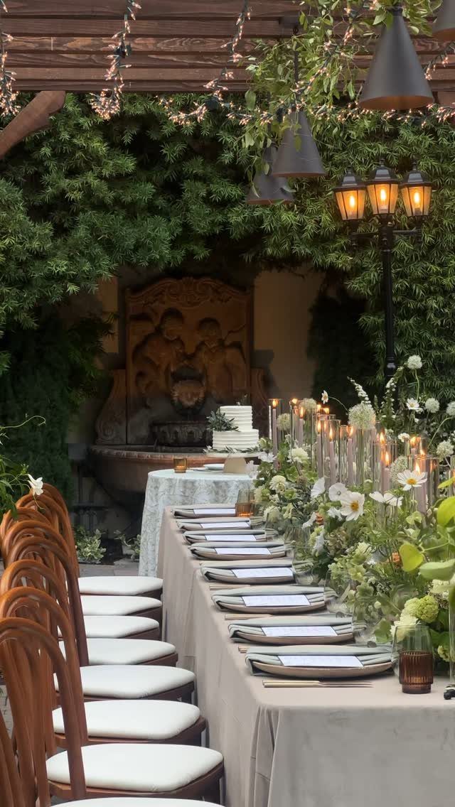 Outdoor wedding reception table with white flowers and wooden chairs under a pergola