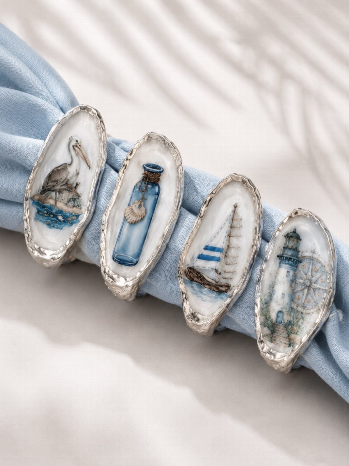 Oyster shell napkin rings with nautical paintings holding a light blue fabric napkin.